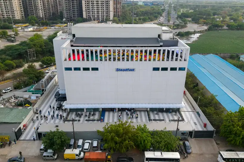 A factory and its blue-roofed sheds photographed from above with fields behind
