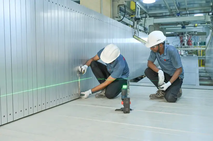 Two engineers in hard hats setting a laser level against a white wall