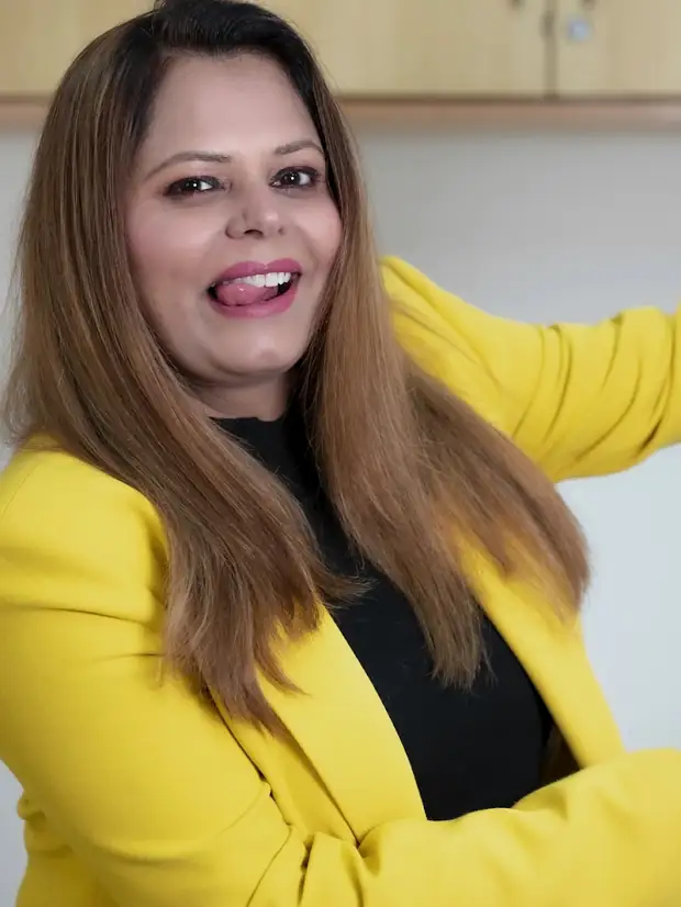 A woman in a yellow blazer photographed against a plain wall