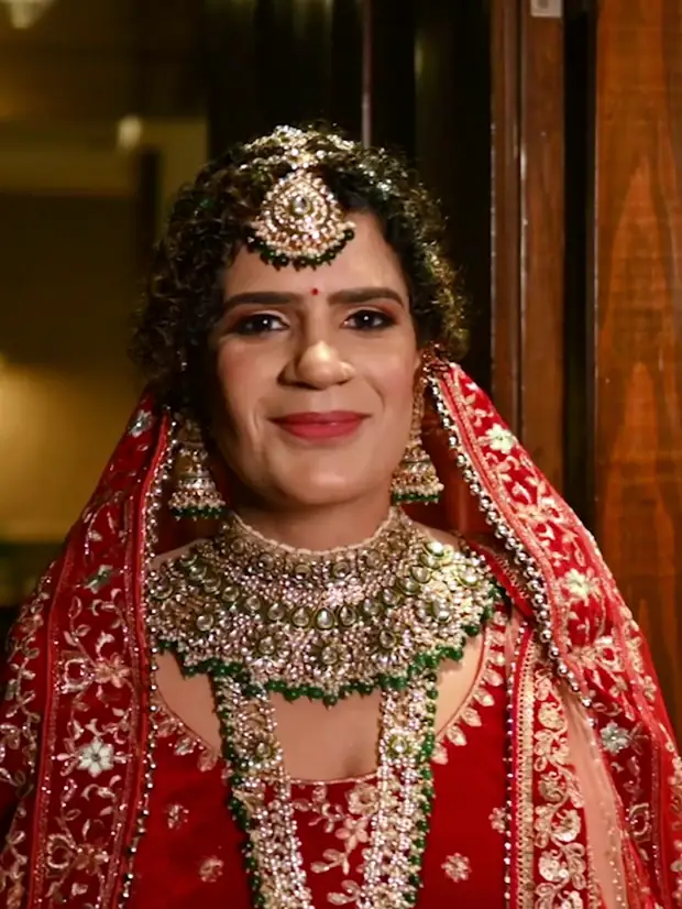 A bride in a red lehenga and gold jewellery, photographed in a doorway