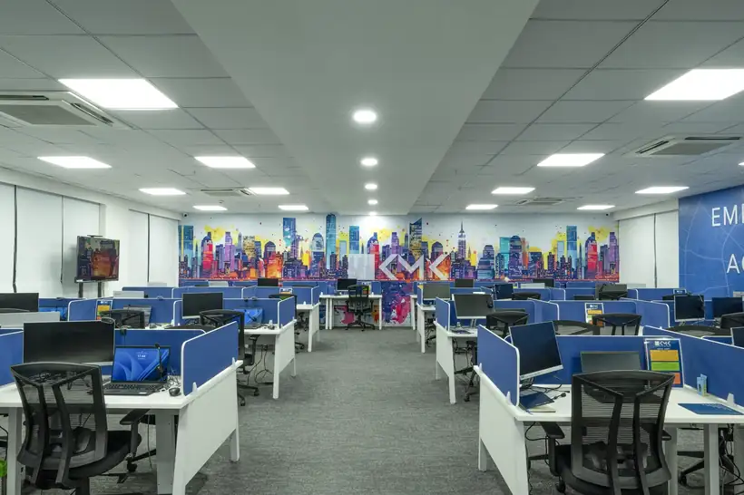 Rows of workstations in front of a printed skyline mural